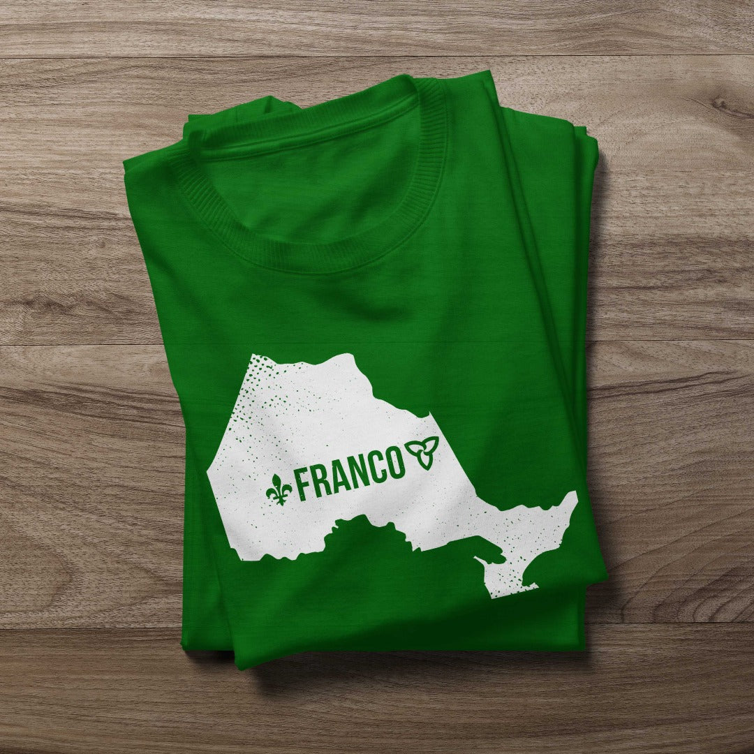 Folded Franco-Ontarian shirt on a wooden background, featuring a design with the silhouette of Ontario, the word "Franco," and the iconic trillium and fleur-de-lys in white print.