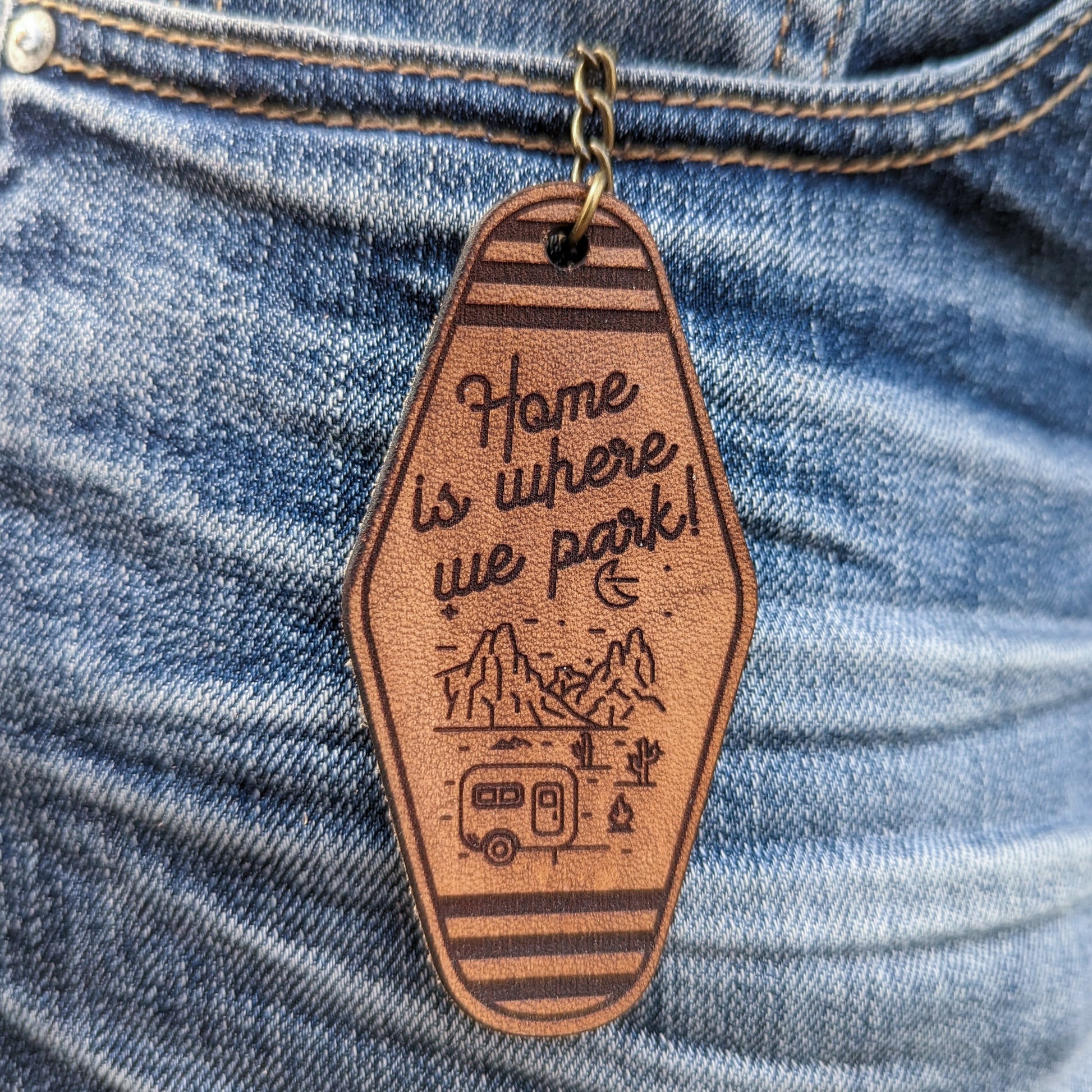 Leather Keychain cut Home is where we park and a line illustration of mountains and an camper engraved on it.