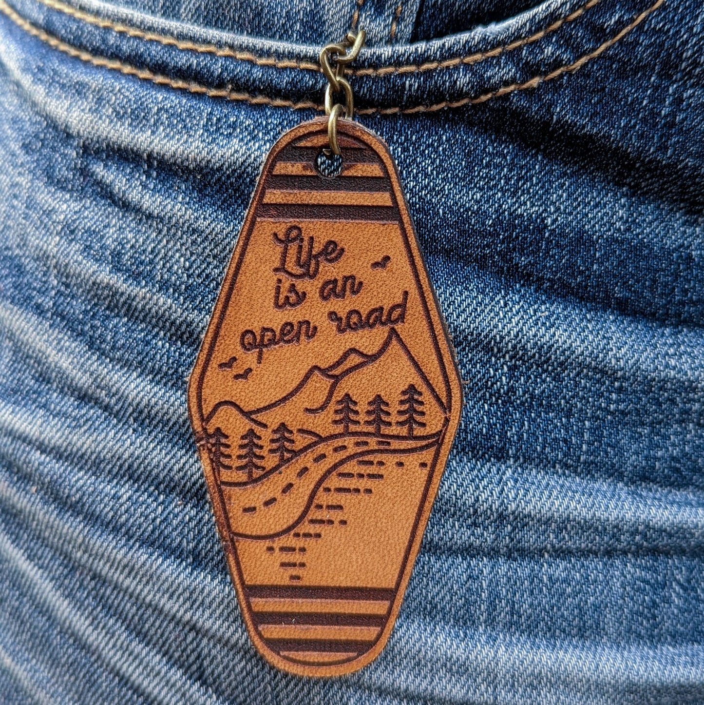 Leather Keychain cut with life is an open road and a mountain road illustration engraved on it.