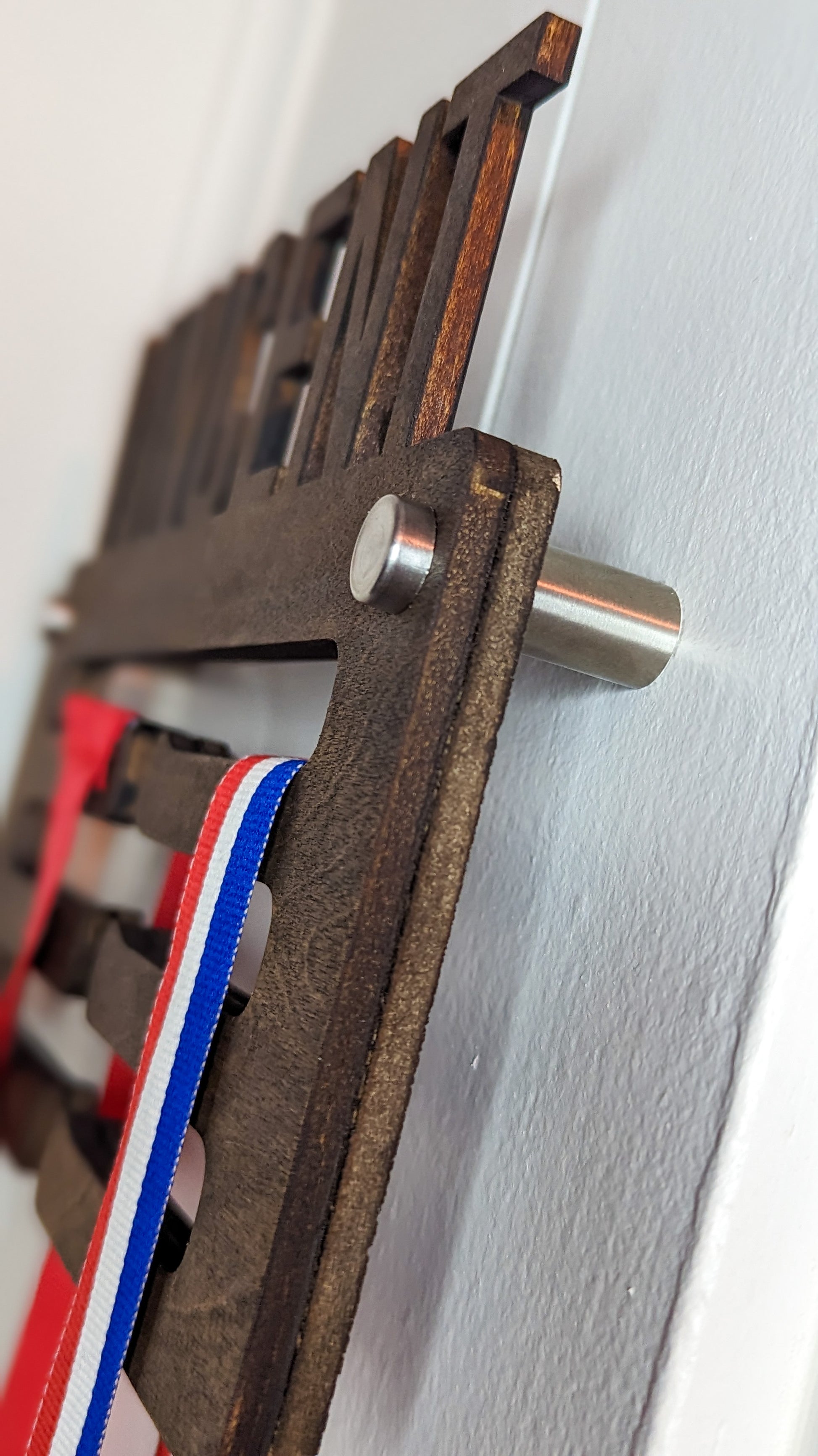 Side view of a dark walnut wooden medal holder highlighting the silver hardware on the wall