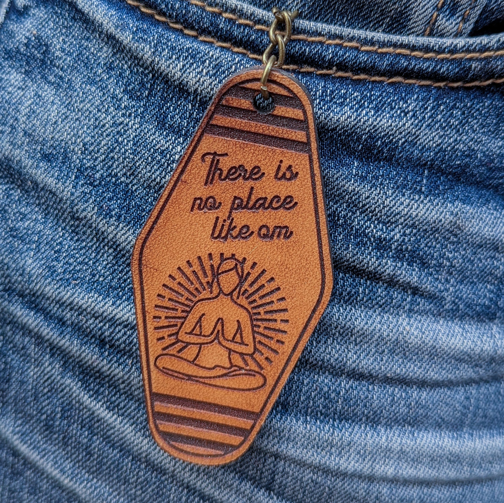 Leather Keychain cut and engraved to look like a vintage motel key with There is no place like om with an illustration of a female figure in a sitting yoga pose engraved on it.